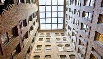 A brick courtyard with tall, windowed walls forming a square, looking up at a skylight ceiling. 140 characters, ending with a period.