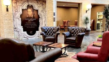 Luxurious indoor lounge with tufted leather chairs, wooden coffee tables, and warm lighting surrounding a framed portrait on a decorative wall.